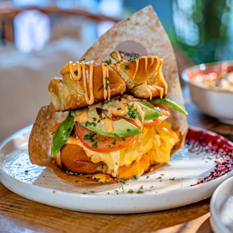 Egg Drop Avo: geröstetes Brioche mit Rührei, Avocado und Tomaten auf einem hellen Teller