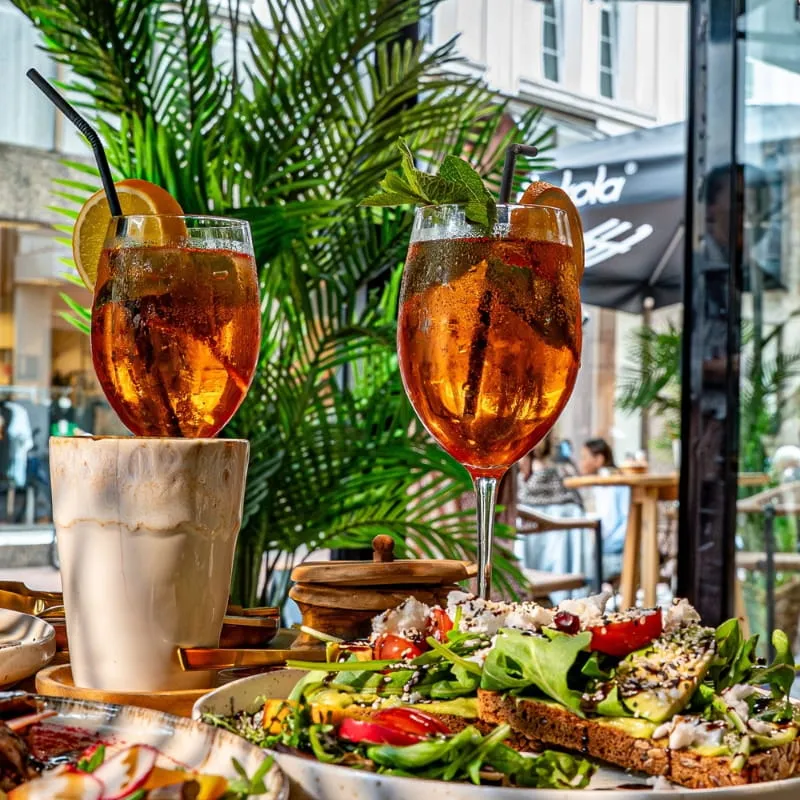 Zwei Aperitifs und ein Eiskaffee neben belegtem Brot mit Salat im Außenbereich