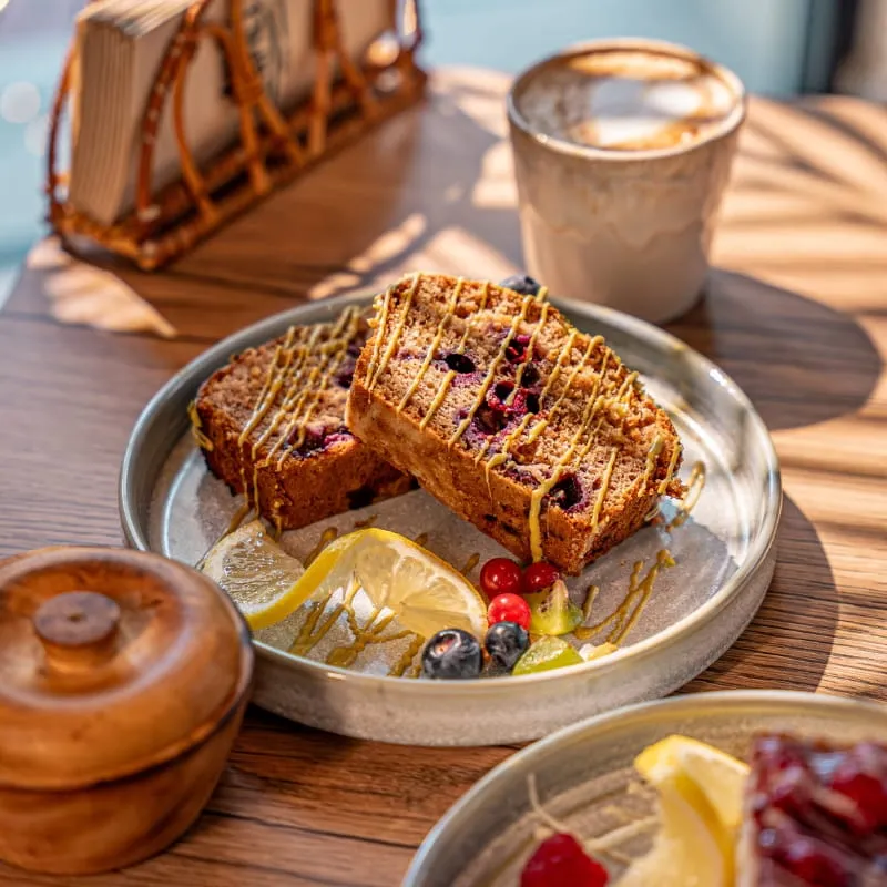Gebäckstücke mit Zitrone und Beeren auf einem Teller, daneben ein Kaffee